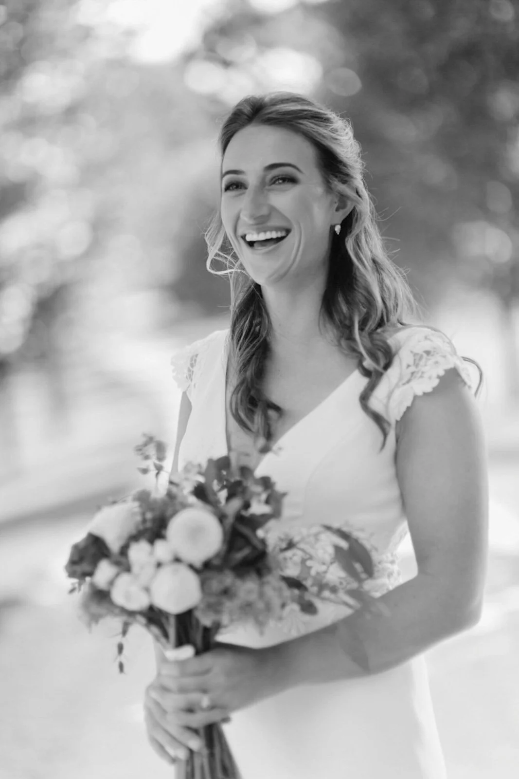 A woman in a wedding dress holding a bouquet of flowers, smiling outdoors.