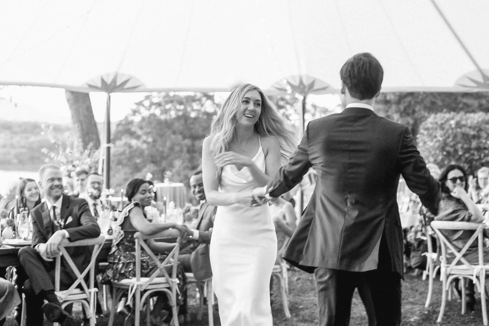 A bride and groom dancing at an outdoor wedding reception with seated guests watching.