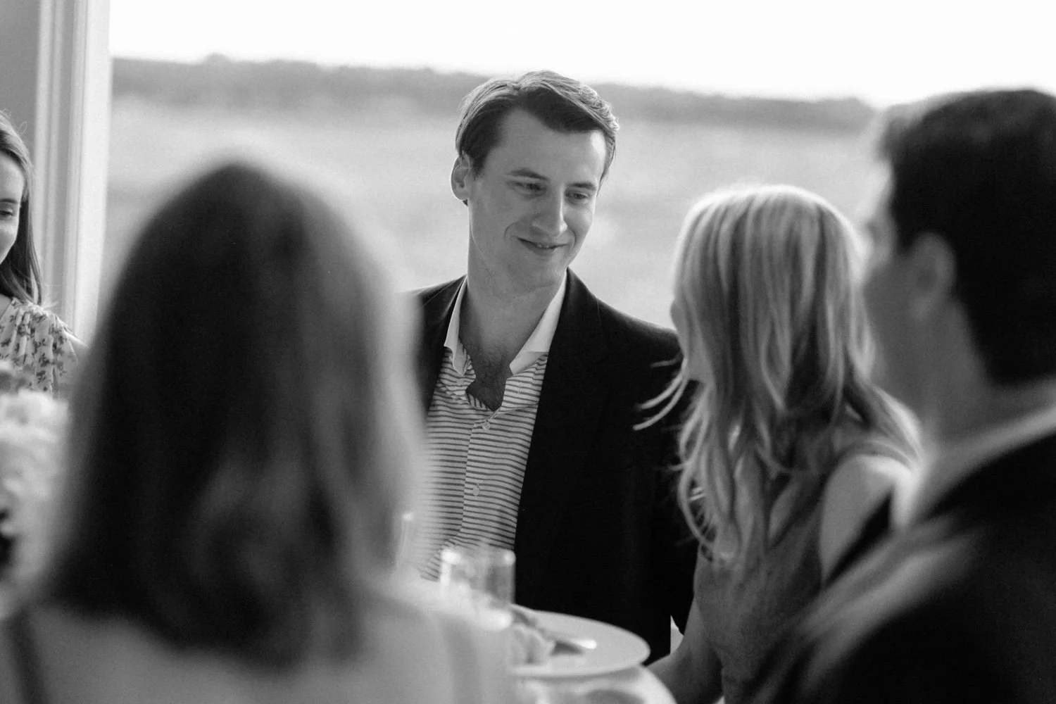 A group of people at a social gathering, with a man smiling and engaging in conversation at The Shinnecock Golf Club.