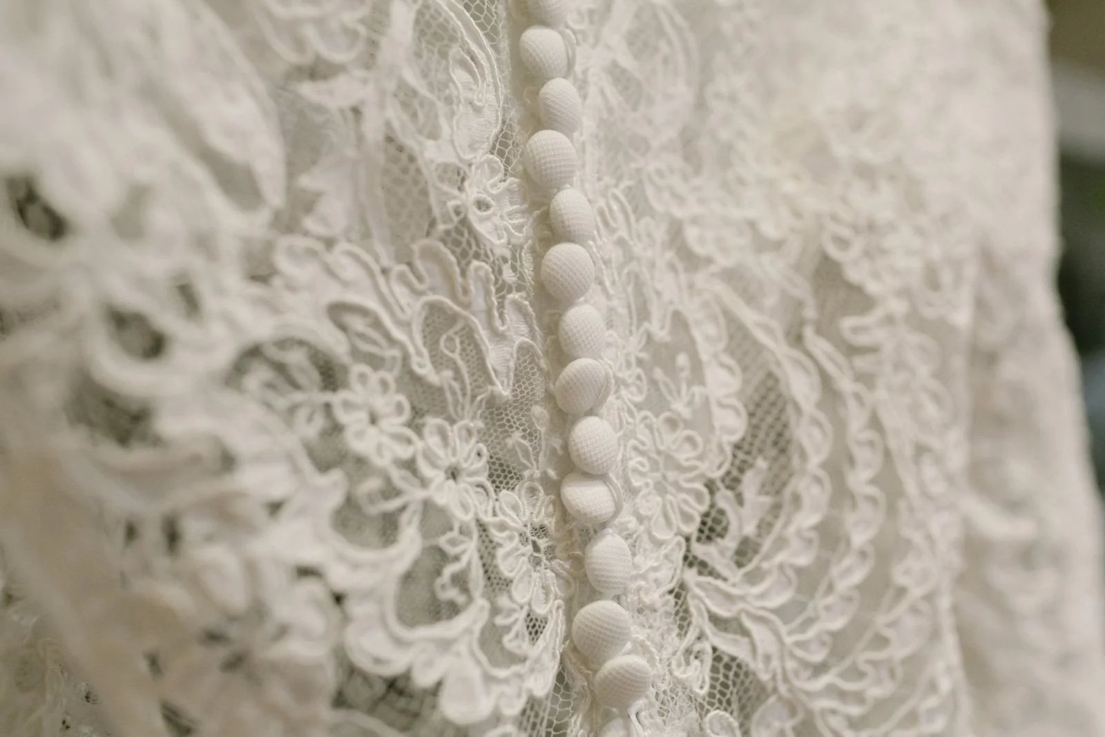 Close-up of a lace fabric with a row of small fabric-covered buttons.