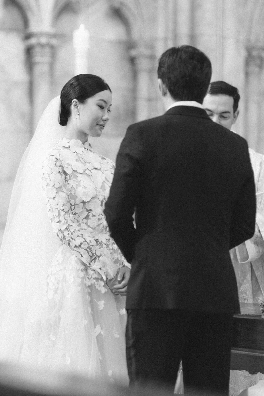 Black and white photo of a wedding ceremony with a bride, groom, and officiant in a church.