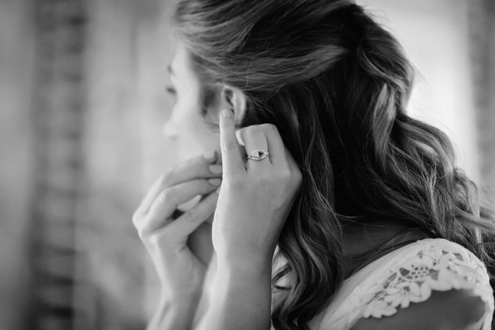 A woman with wavy hair is touching her ear, wearing a ring on her finger, and appears to be lost in thought.