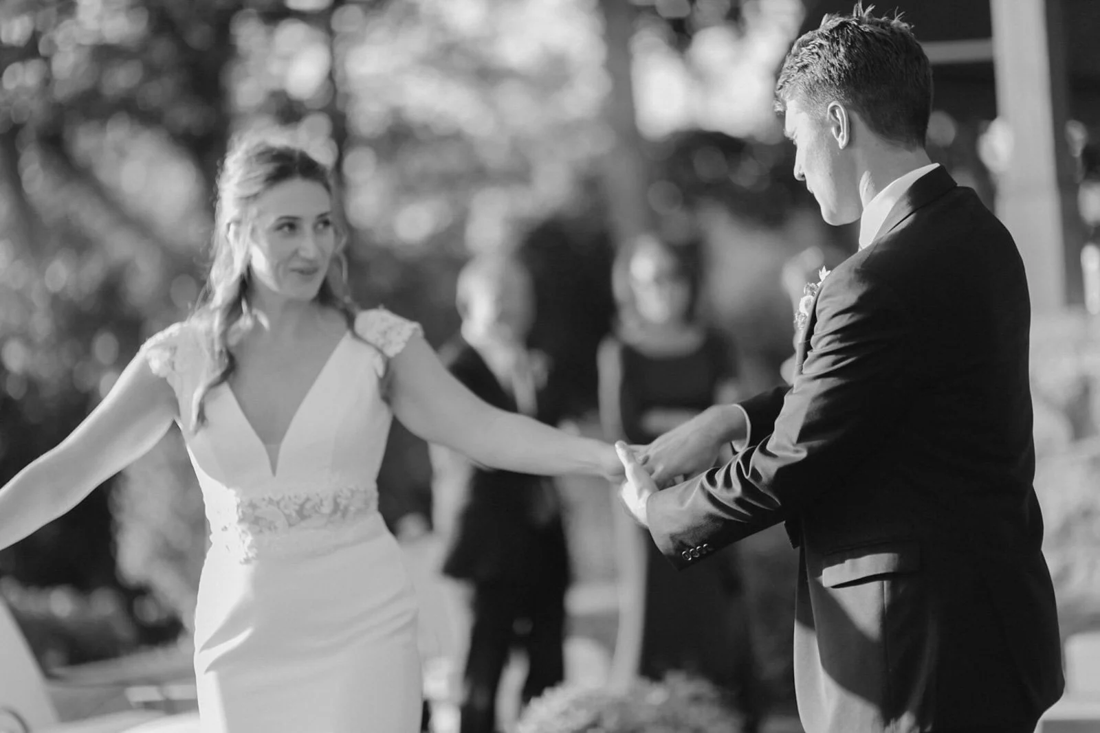 A bride and groom holding hands during a wedding ceremony outdoors in black and white.