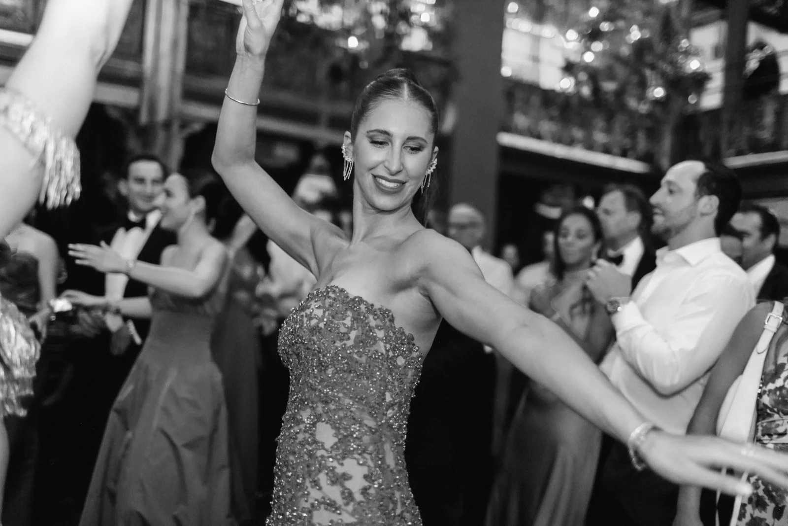 A woman in an ornate dress is dancing at a formal event surrounded by an audience of well-dressed people.