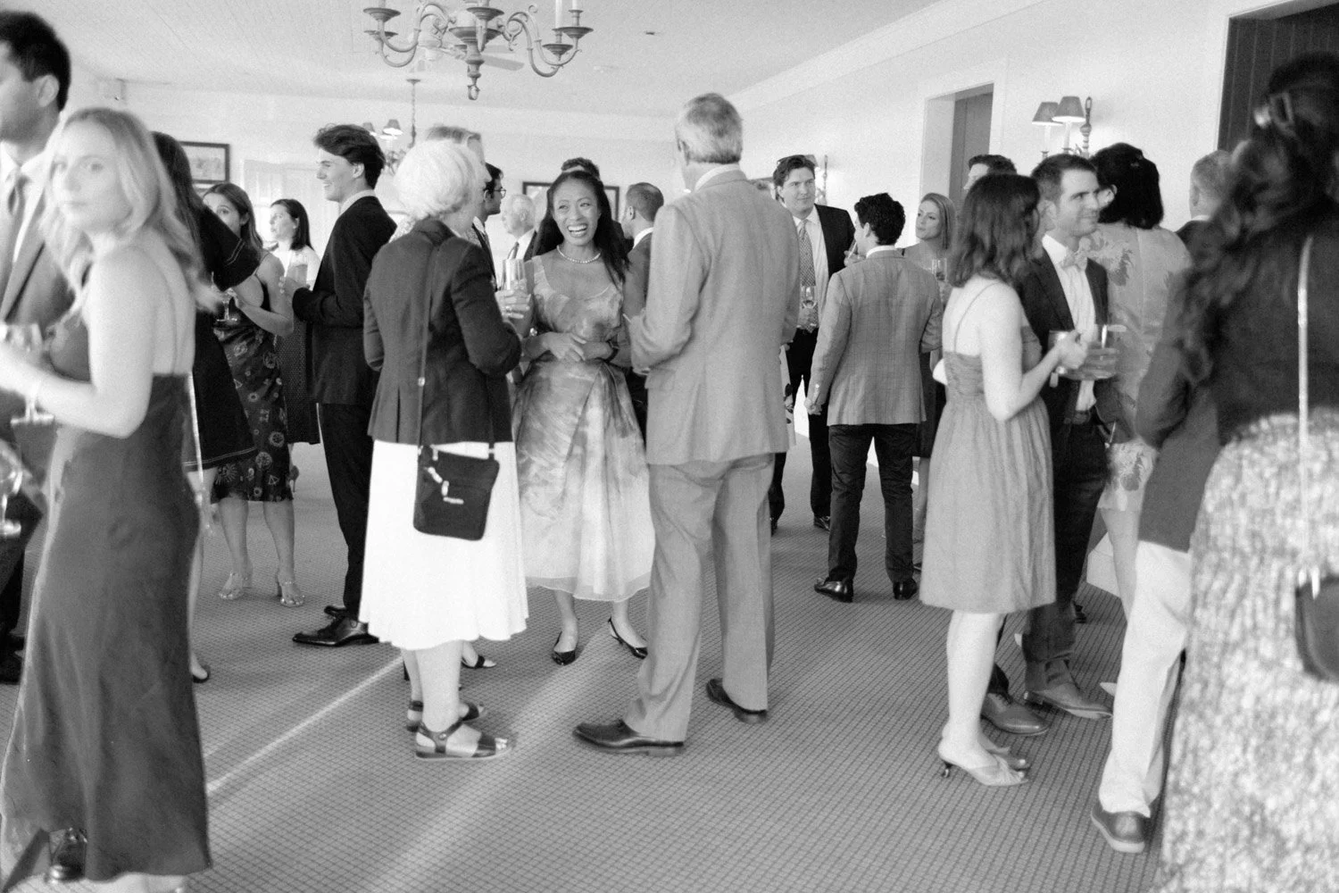 People attending a social gathering or party in an indoor setting, dressed in formal or semi-formal attire, talking and holding drinks.