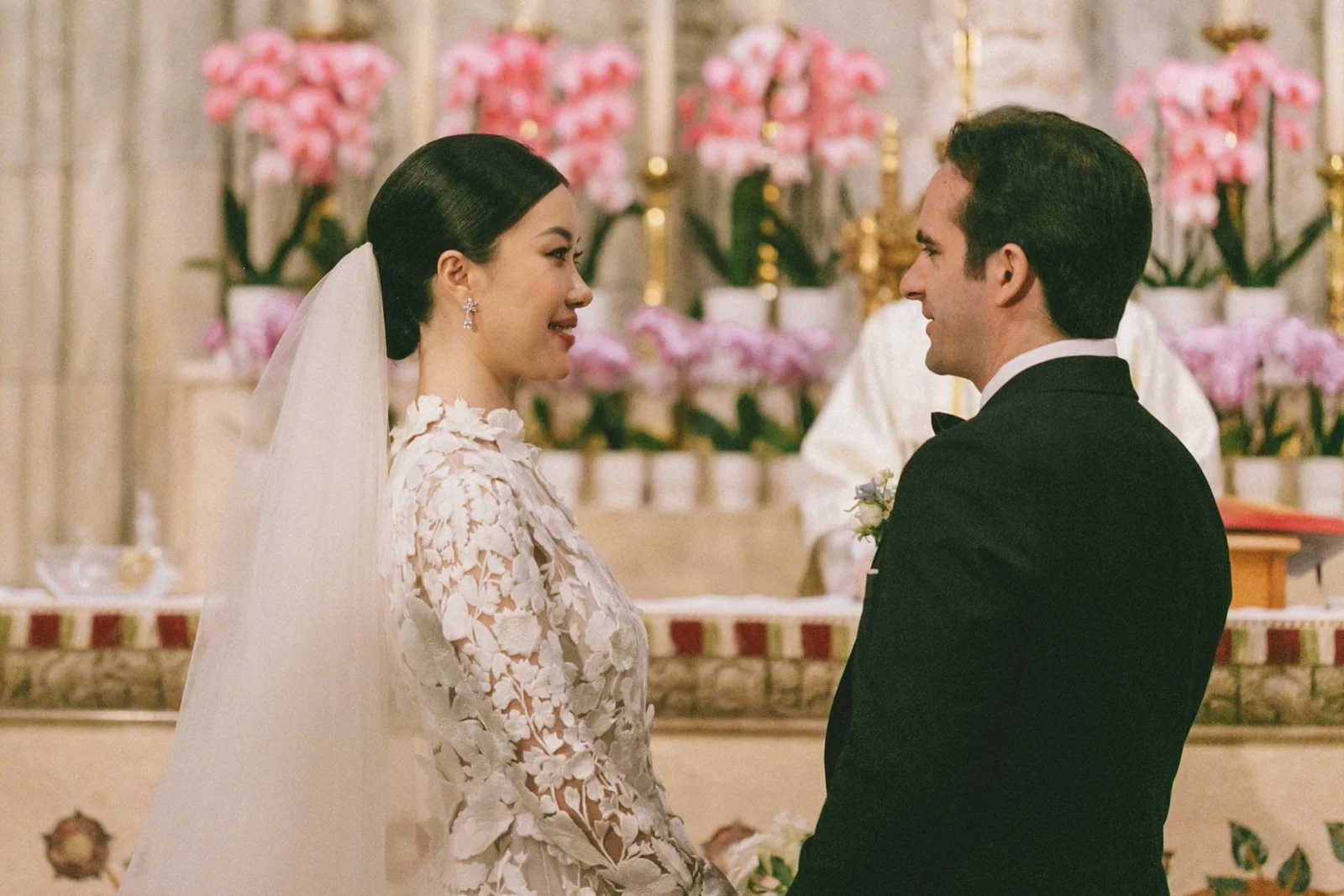 A bride and groom standing face to face during wedding vows inside a decorated church.