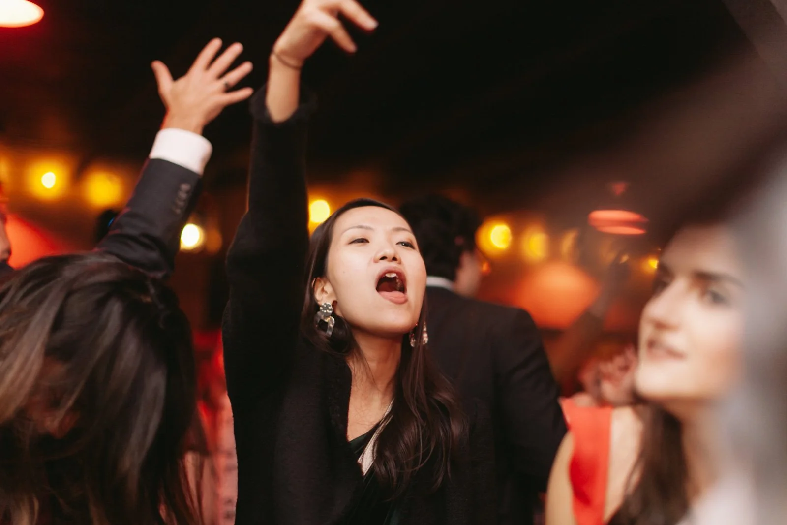 A woman singing and dancing at a party with friends in a dimly lit venue.