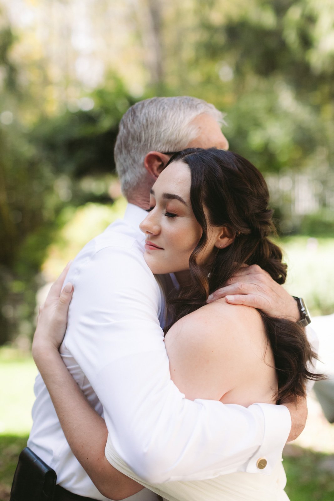 A man and woman hugging outdoors, with their eyes closed and smiling softly.