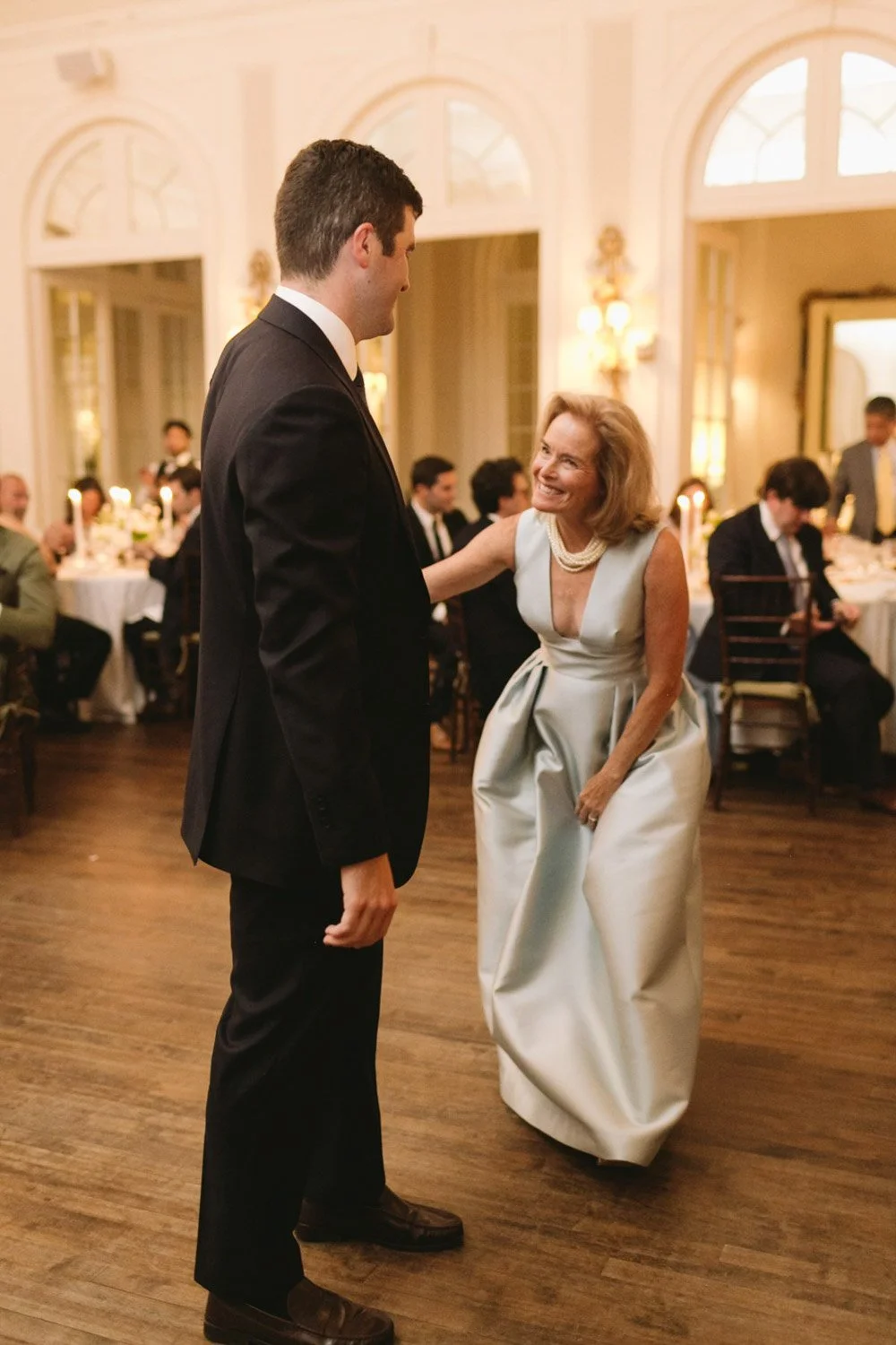 A woman in a white gown dancing and smiling with a man in a black suit at a formal event or wedding reception.