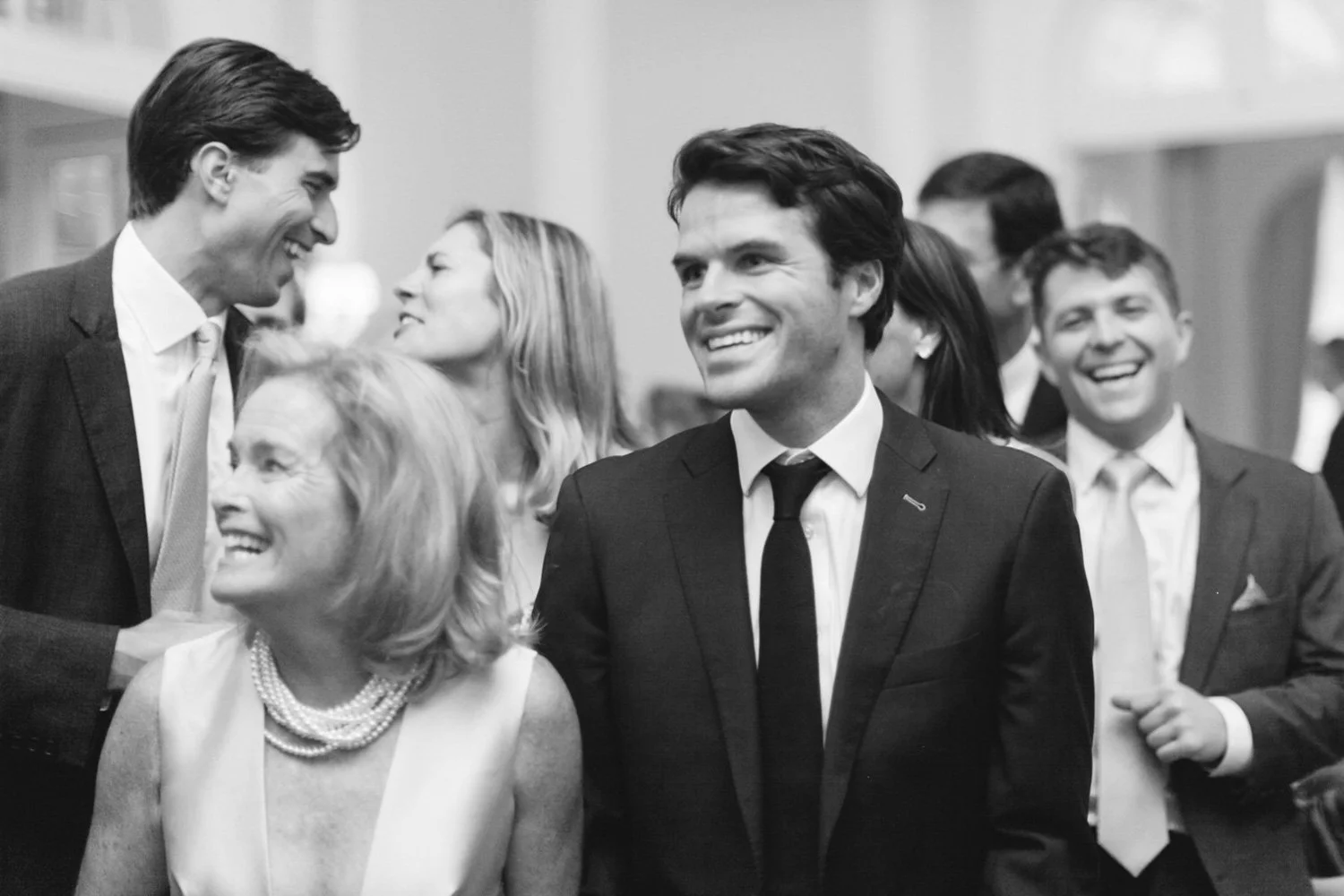 Group of professionally dressed men and women laughing and socializing at an indoor event.