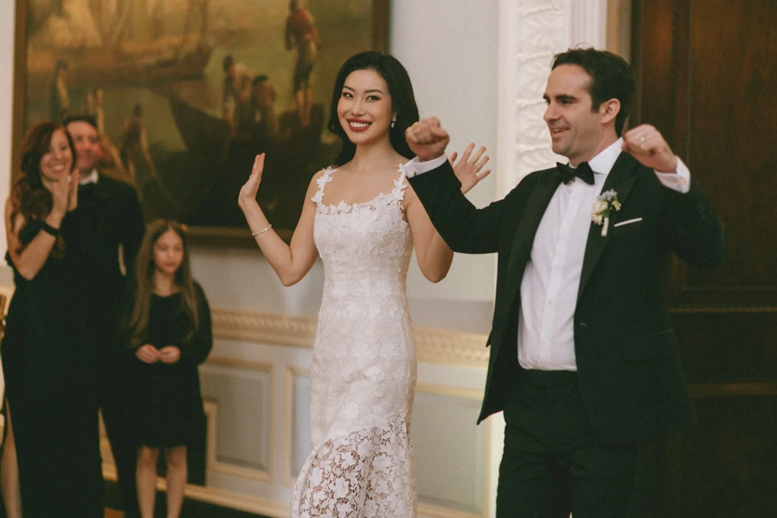 A bride and groom dancing at their wedding reception with guests clapping and watching in the background.