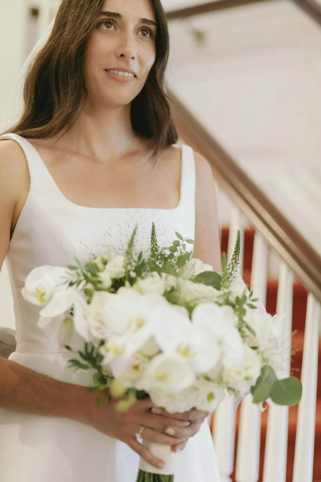 A young woman in a white dress holding a bouquet of white and green flowers.