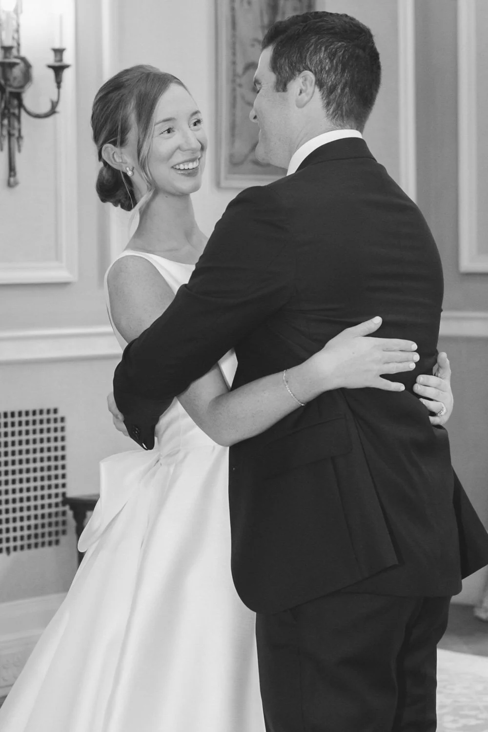 A bride and groom sharing a dance at their wedding reception, gazing at each other with smiles, in a decorated room.