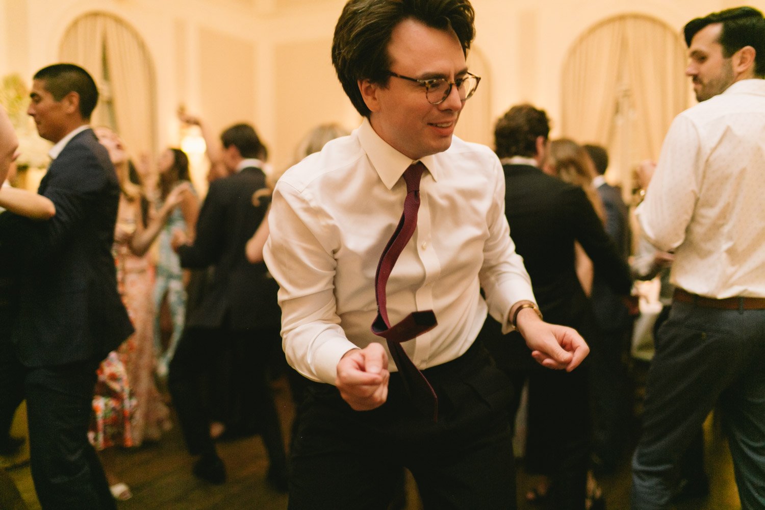 Person dancing at a formal event or party with other people in the background.