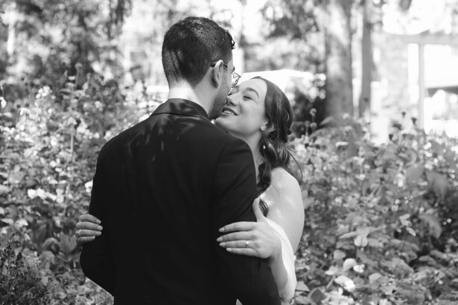 A couple dressed in wedding attire embracing outdoors, smiling and sharing a romantic moment.
