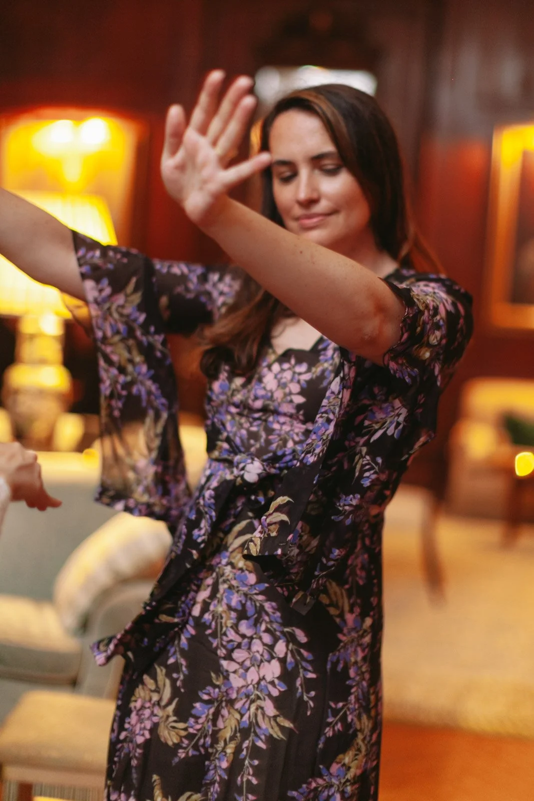 A woman in a floral dress dancing with her eyes closed and her hand raised.