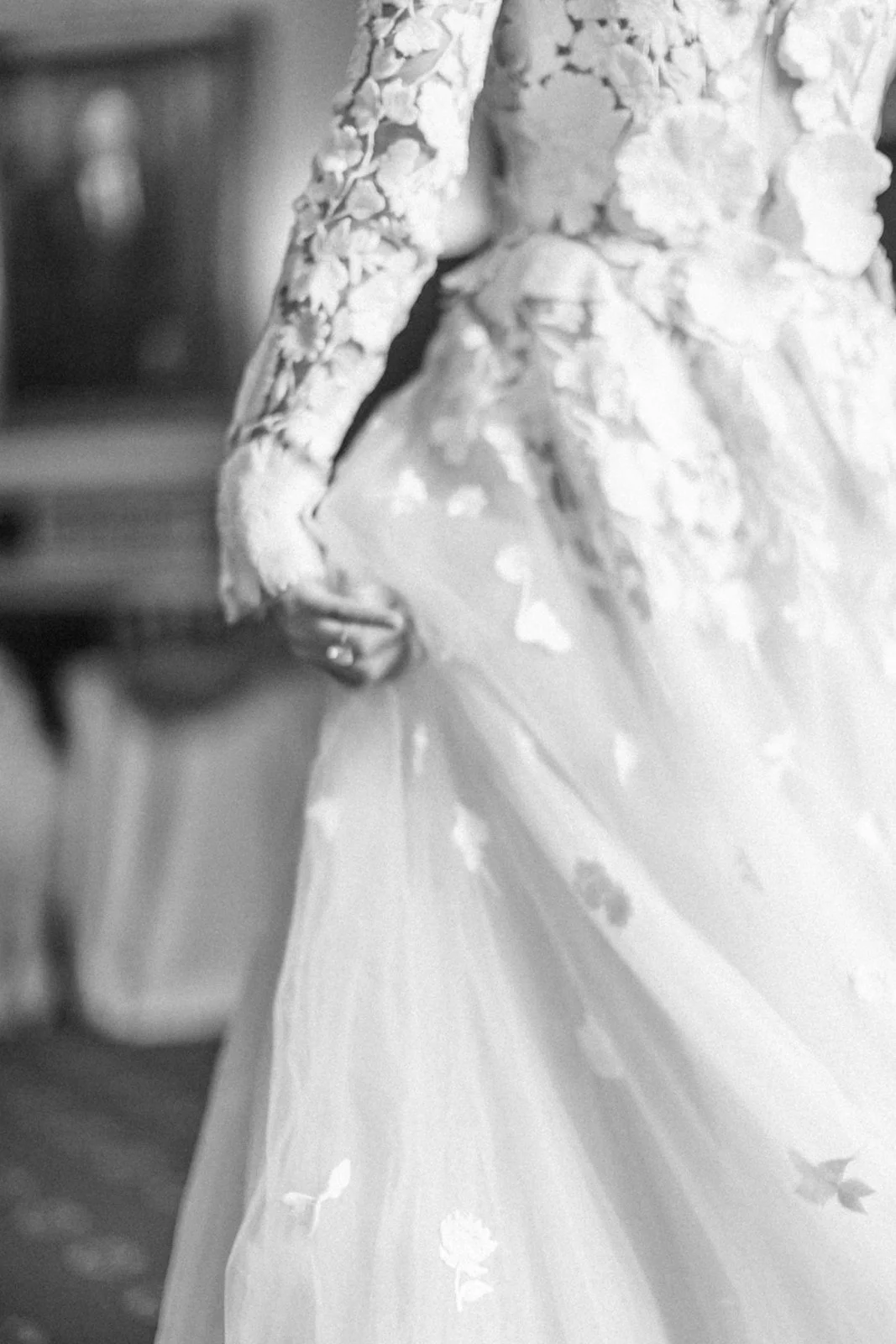 Close-up of a bride in a wedding gown with lace sleeves and a full tulle skirt, holding the edge of her dress.