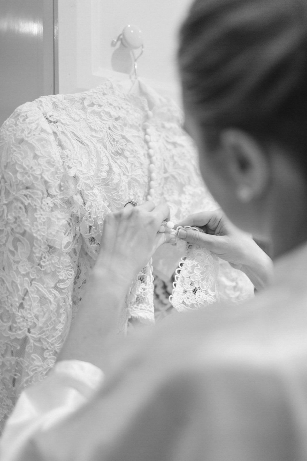 A person in lace clothing is holding a string of pearls, with another person assisting, in a black-and-white photo.
