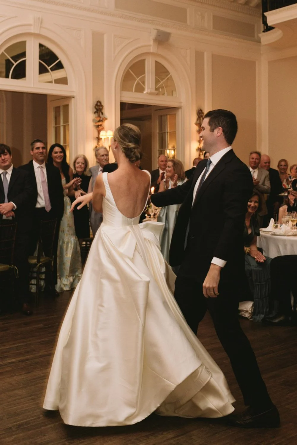 Bride and groom dancing at wedding reception with seated guests watching.