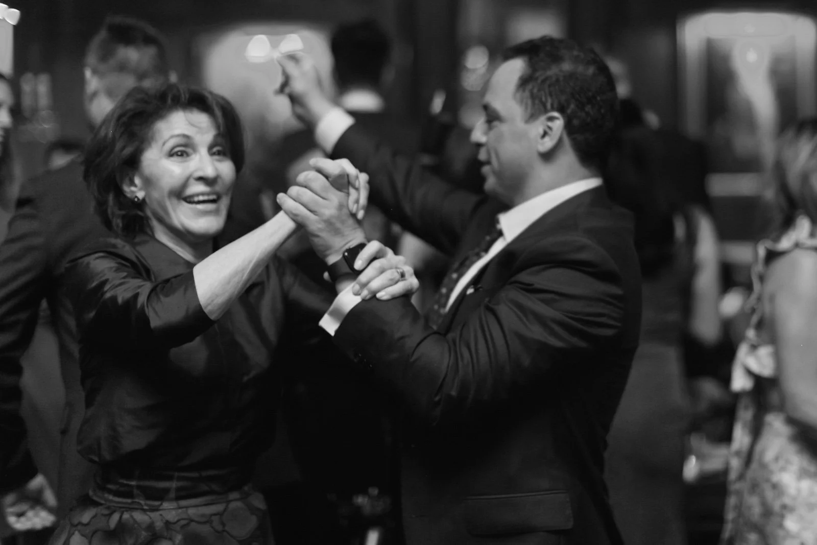 A black and white photo of a woman and a man dancing together at a social event, smiling and holding hands.