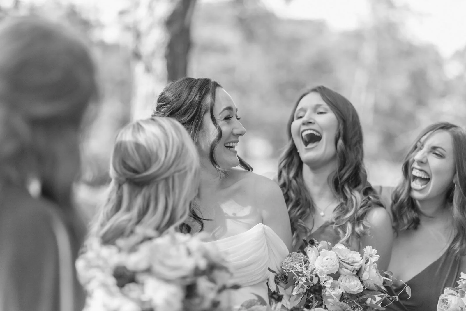 Black and white photo of a bride and three women celebrating outdoors, smiling and laughing.