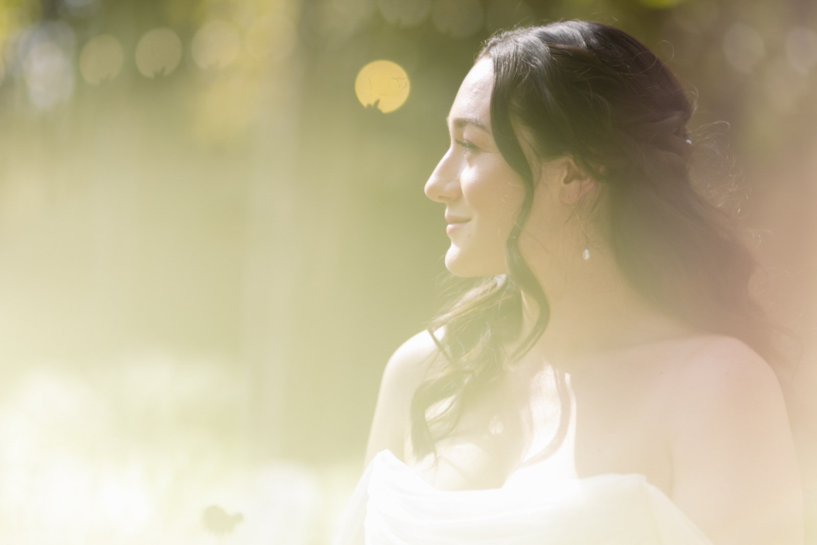 Profile of a woman with dark hair in loose waves, enjoying sunlight outdoors, with soft focus and a warm, dreamy atmosphere.
