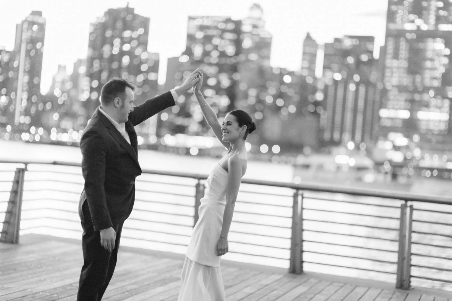 A couple dancing on a waterfront promenade at night with city skyline in the background.