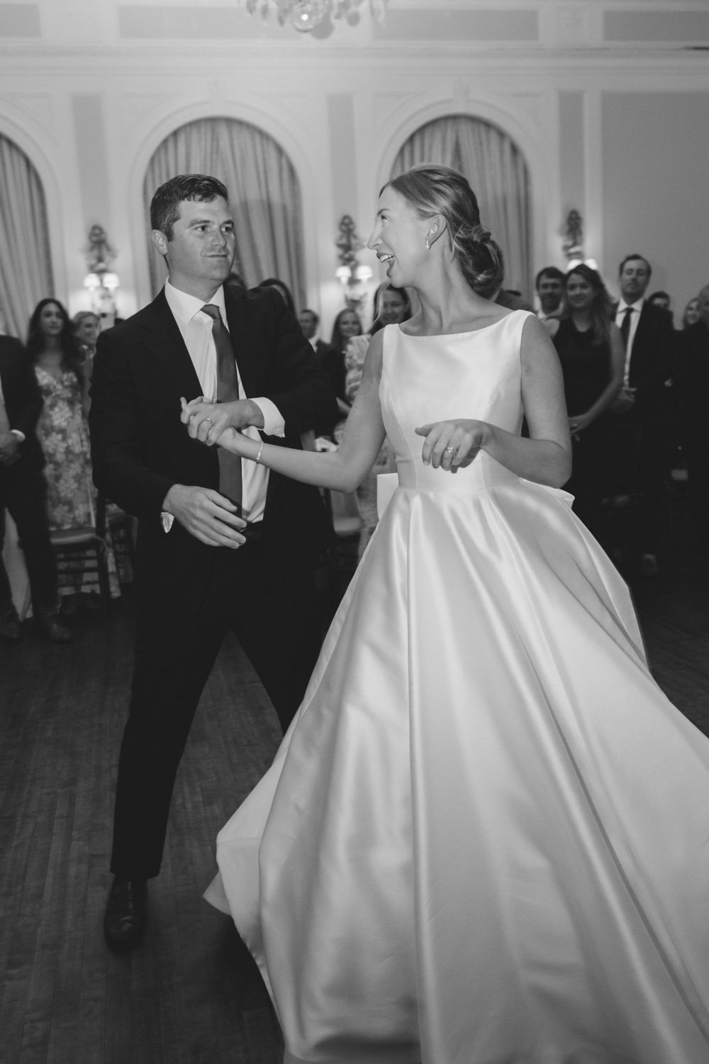 A bride and groom are dancing at their wedding reception, surrounded by guests in an elegant ballroom.