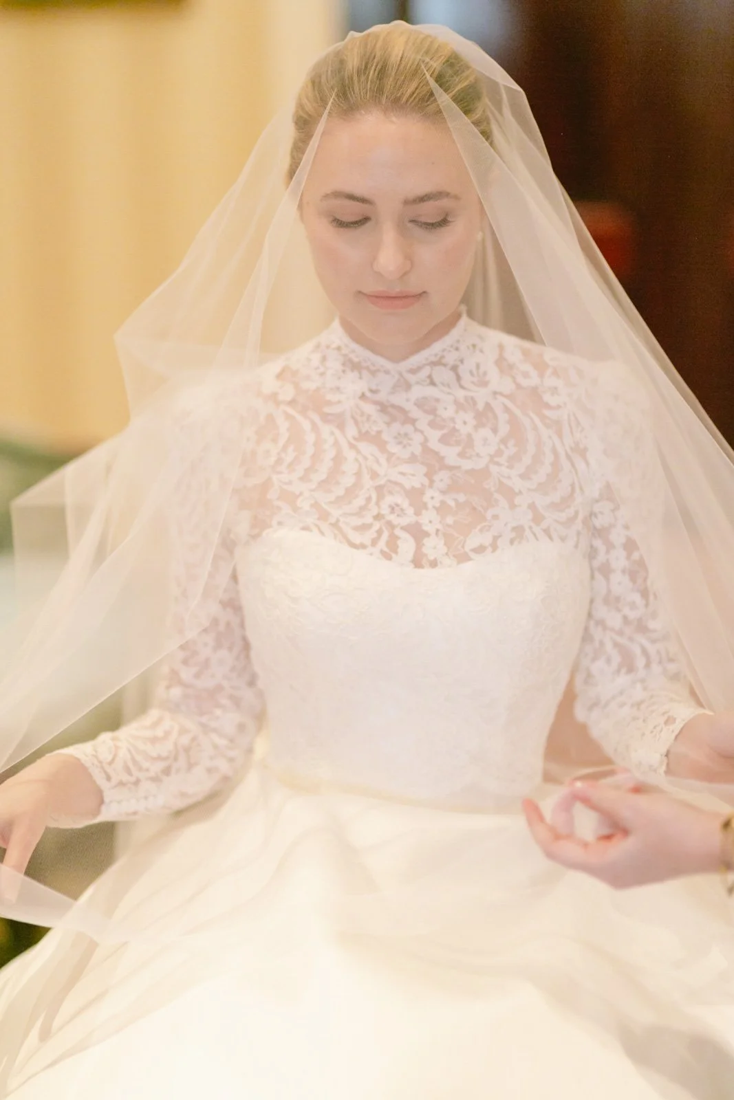 A bride in a lace wedding dress and veil, looking down quietly.