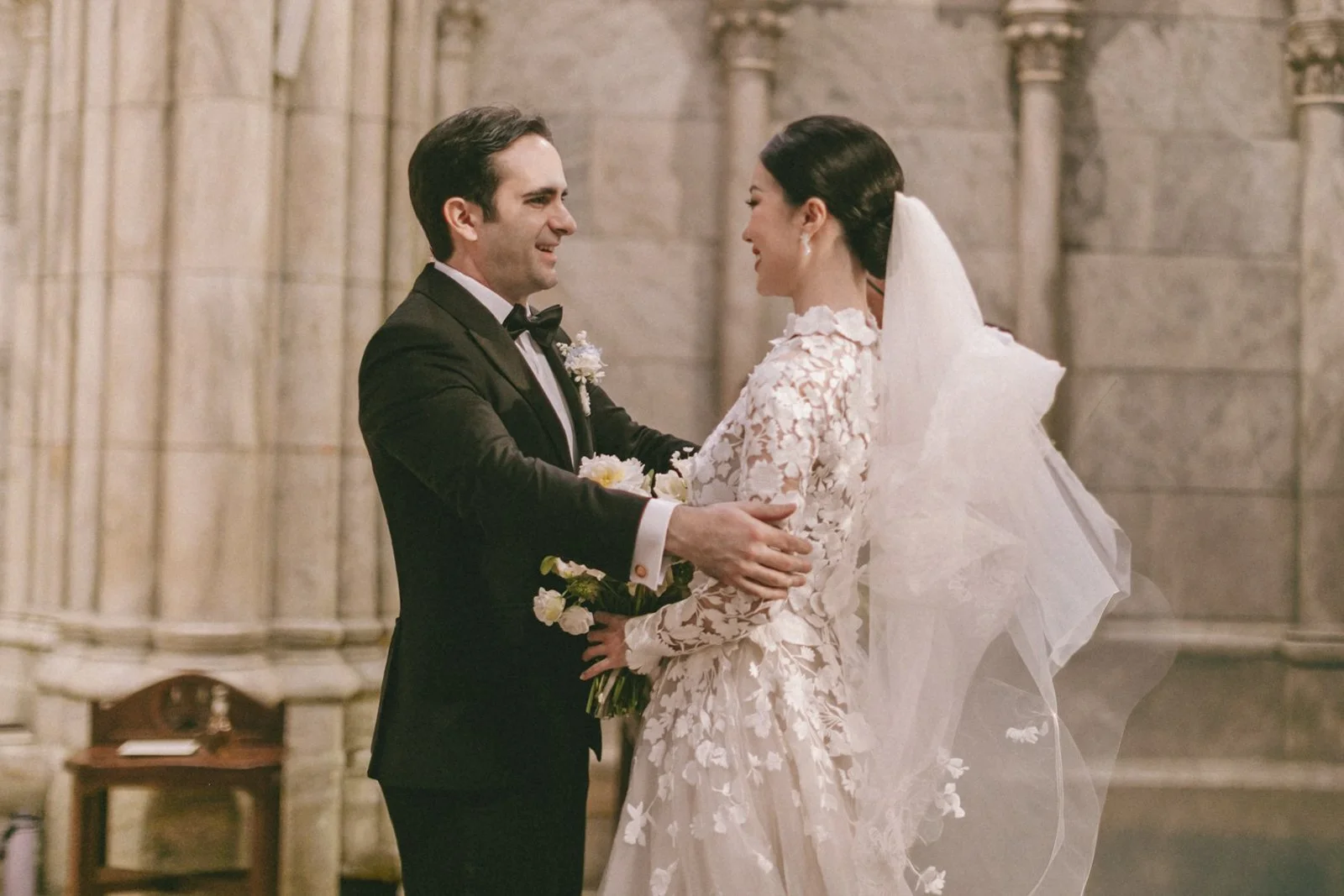 A bride and groom exchanging vows inside a church, with stone walls and an altar in the background.