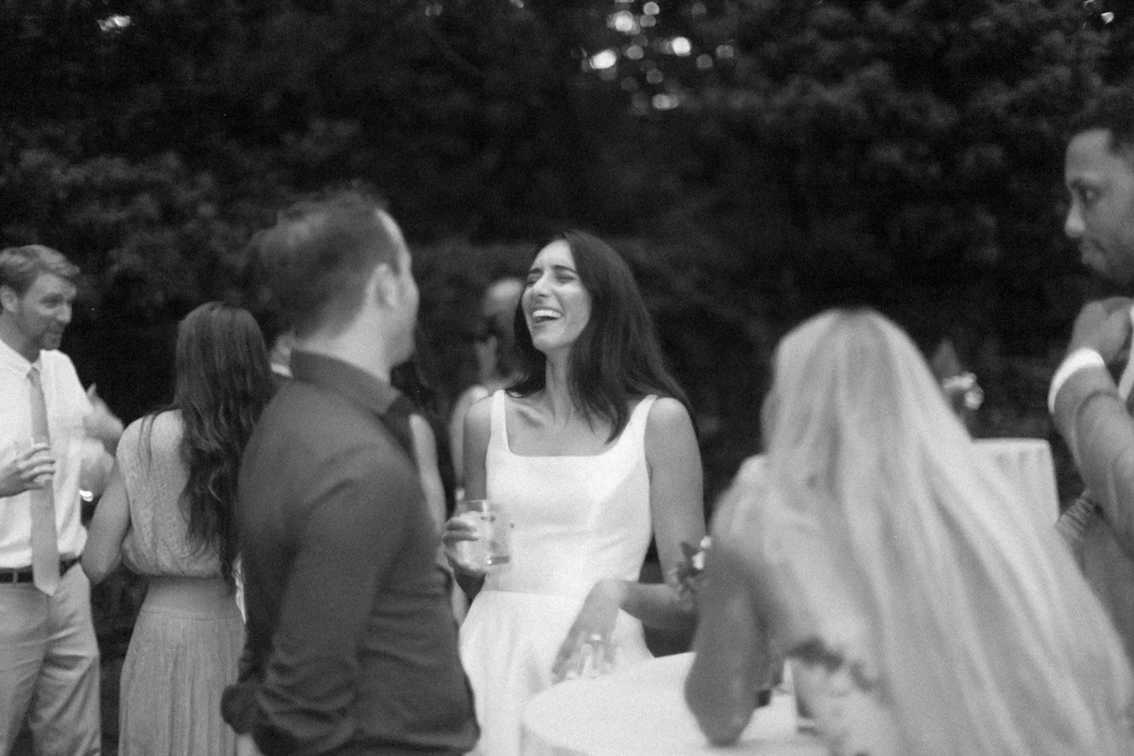 People socializing at an outdoor event, a woman in a white dress is sharing a laugh with a group of men and women.