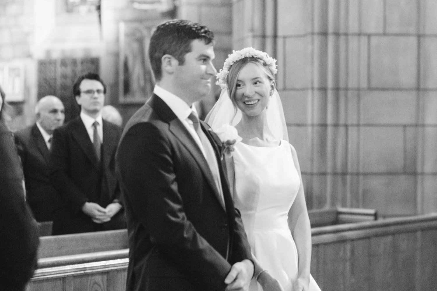 A bride and groom exchanging vows in a church during their wedding ceremony, with guests observing in the background.