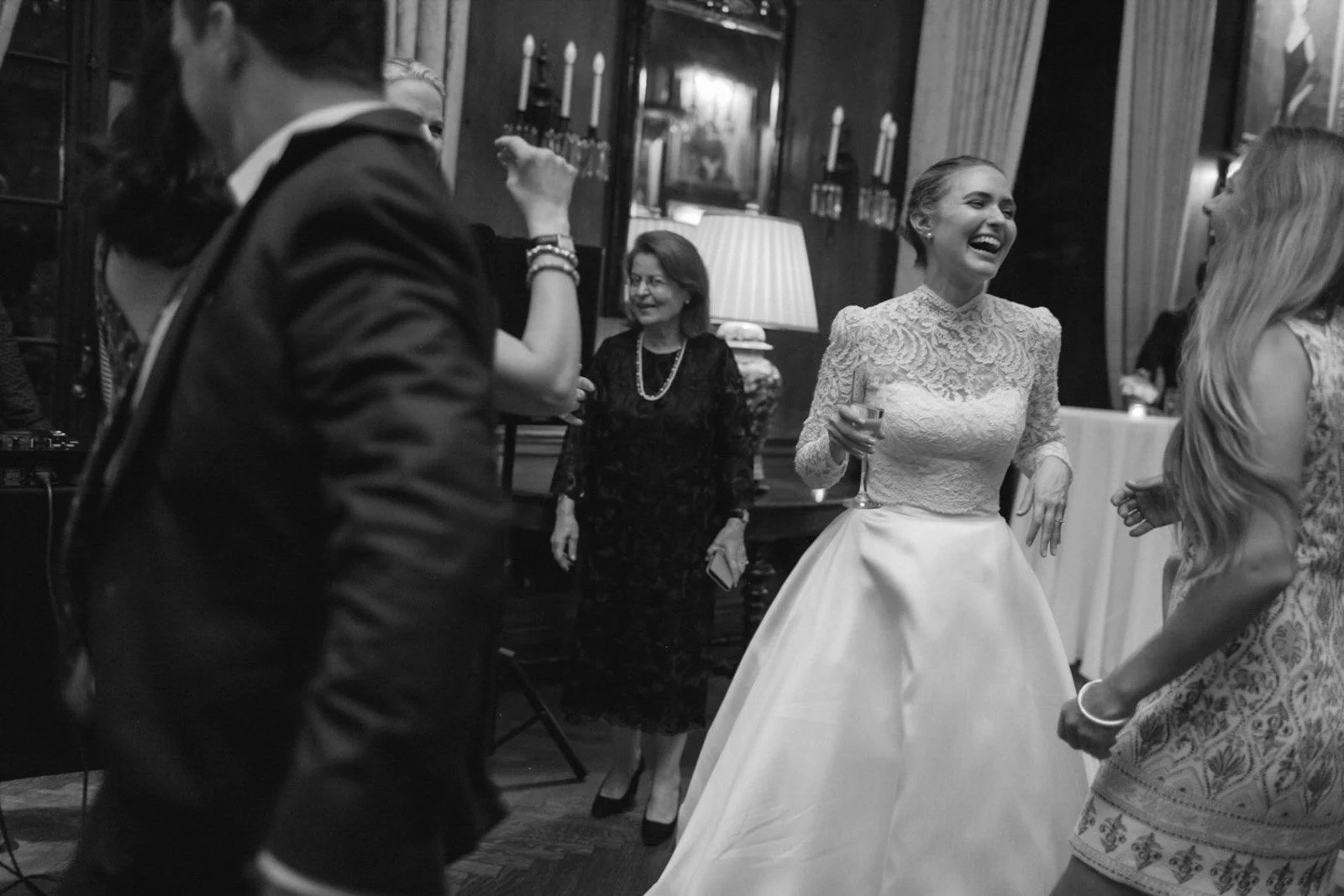 Black and white photo of women dancing and socializing at an event, with decorations and candle holders in the background.