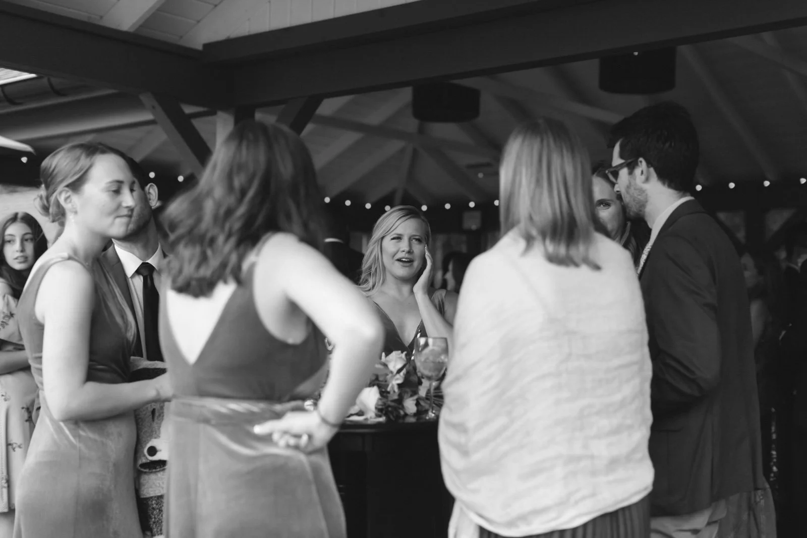 Group of people socializing at an indoor event, with a woman in the center showing a surprised or confused expression.