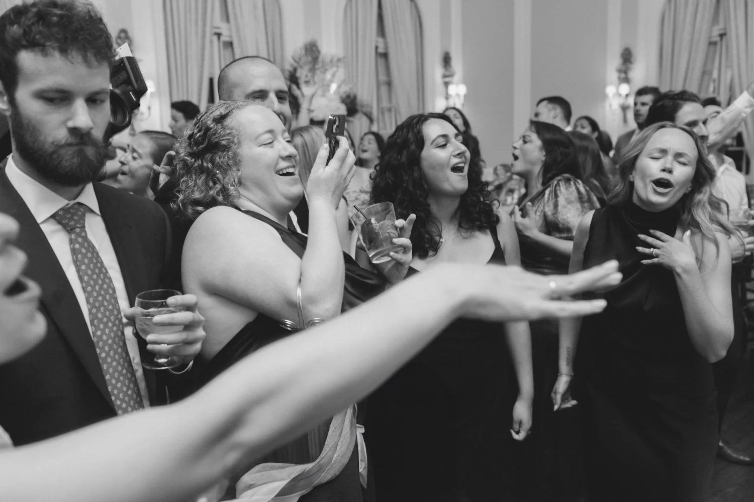 Group of people at a social gathering, smiling, singing, and dancing in a decorated room, some holding drinks.