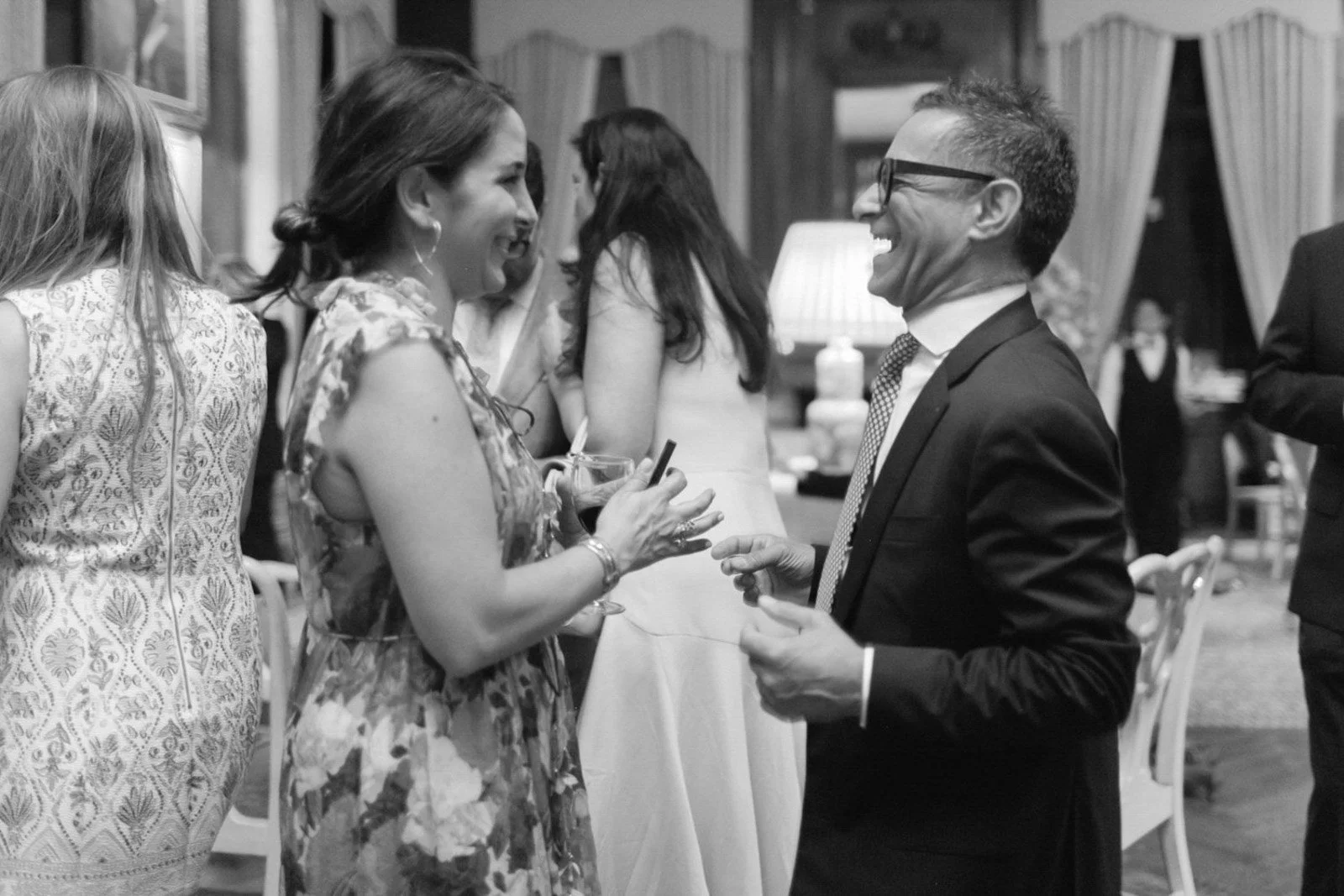 People enjoying conversation and drinks at a social gathering, likely a formal event or party, in a decorated indoor setting.