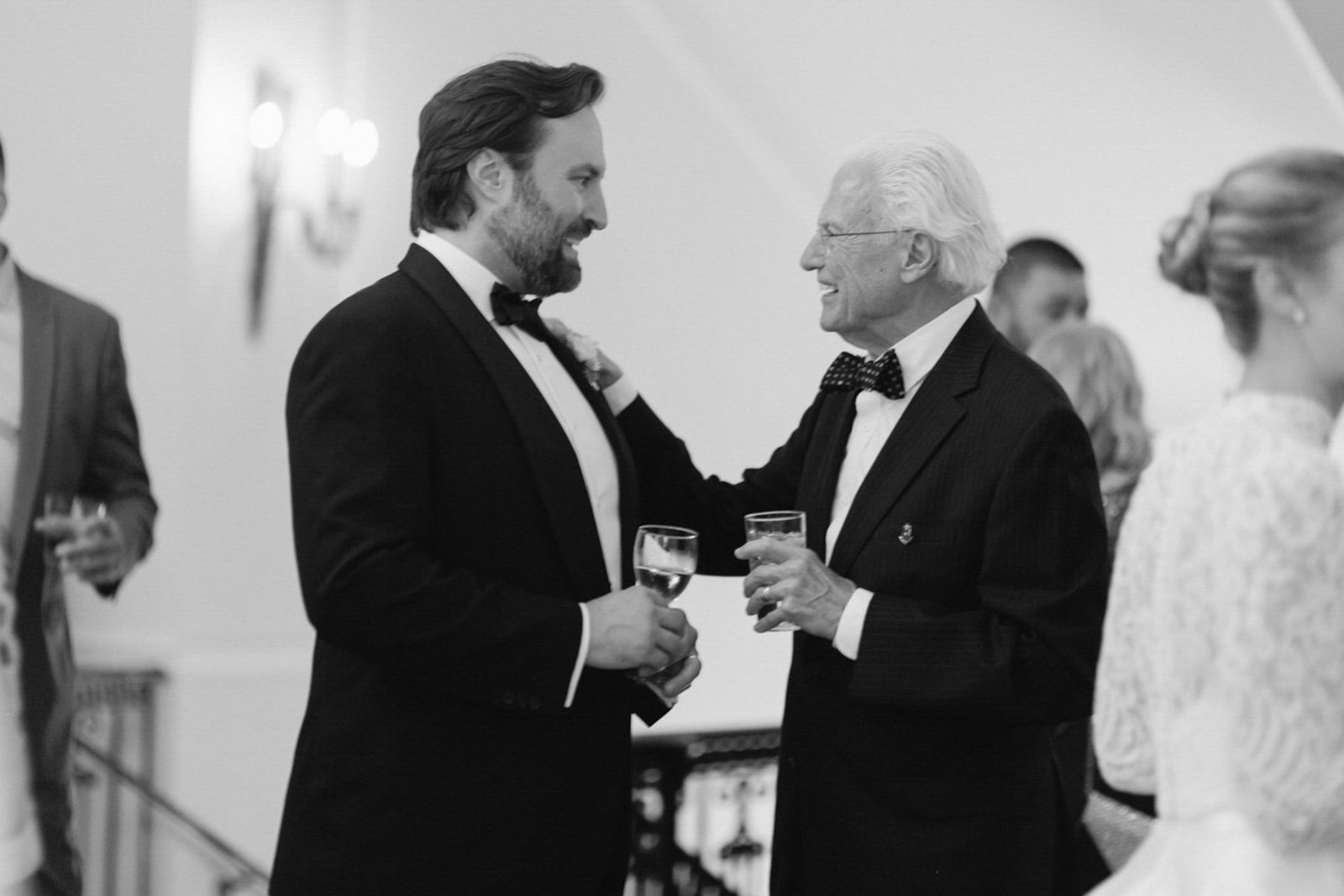 Two men in tuxedos sharing a toast and smiling at each other during a formal event.