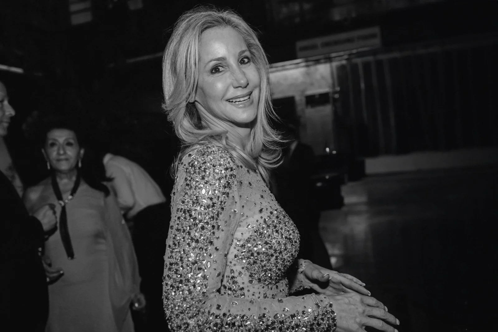 Black and white photo of a woman with shoulder-length hair, wearing a sequined dress, smiling and facing slightly to the right.