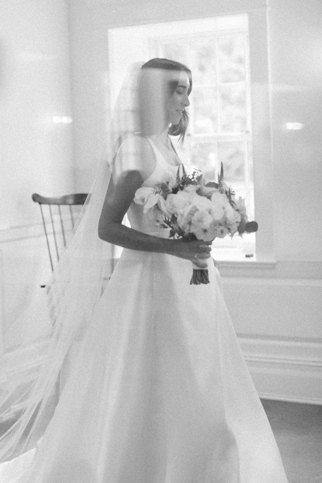 Black and white photo of a bride holding a bouquet, seen through a window or reflective surface