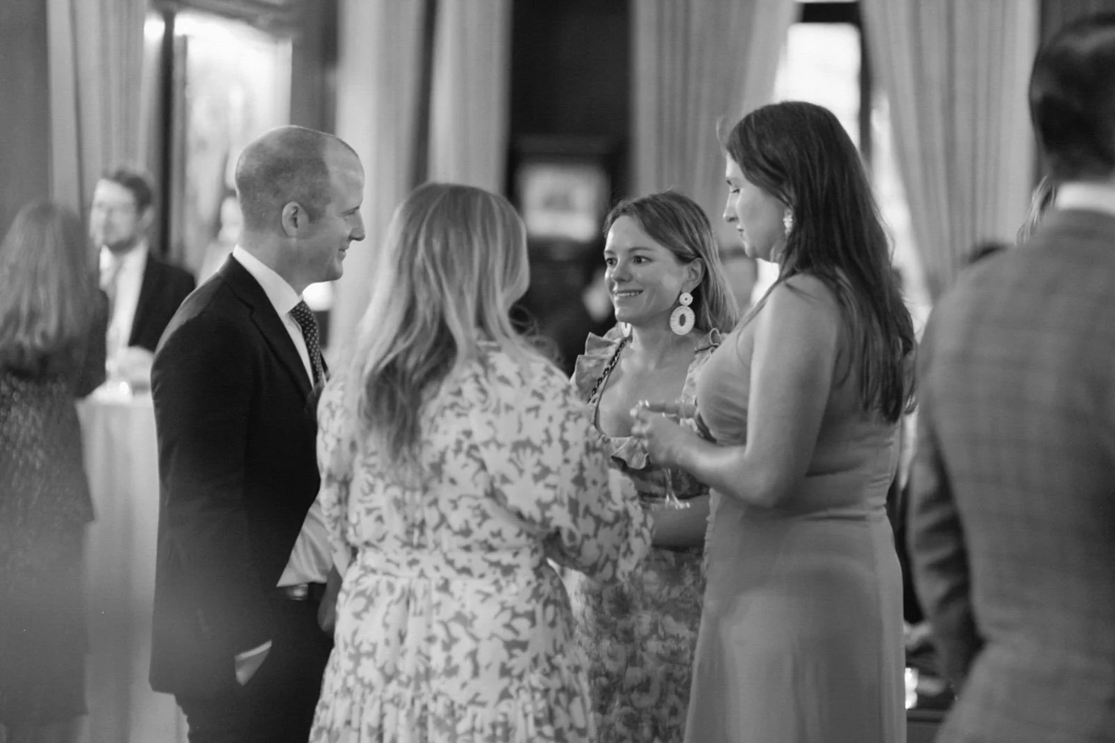 People socializing at a formal event or party, engaged in conversation, with some holding drinks.