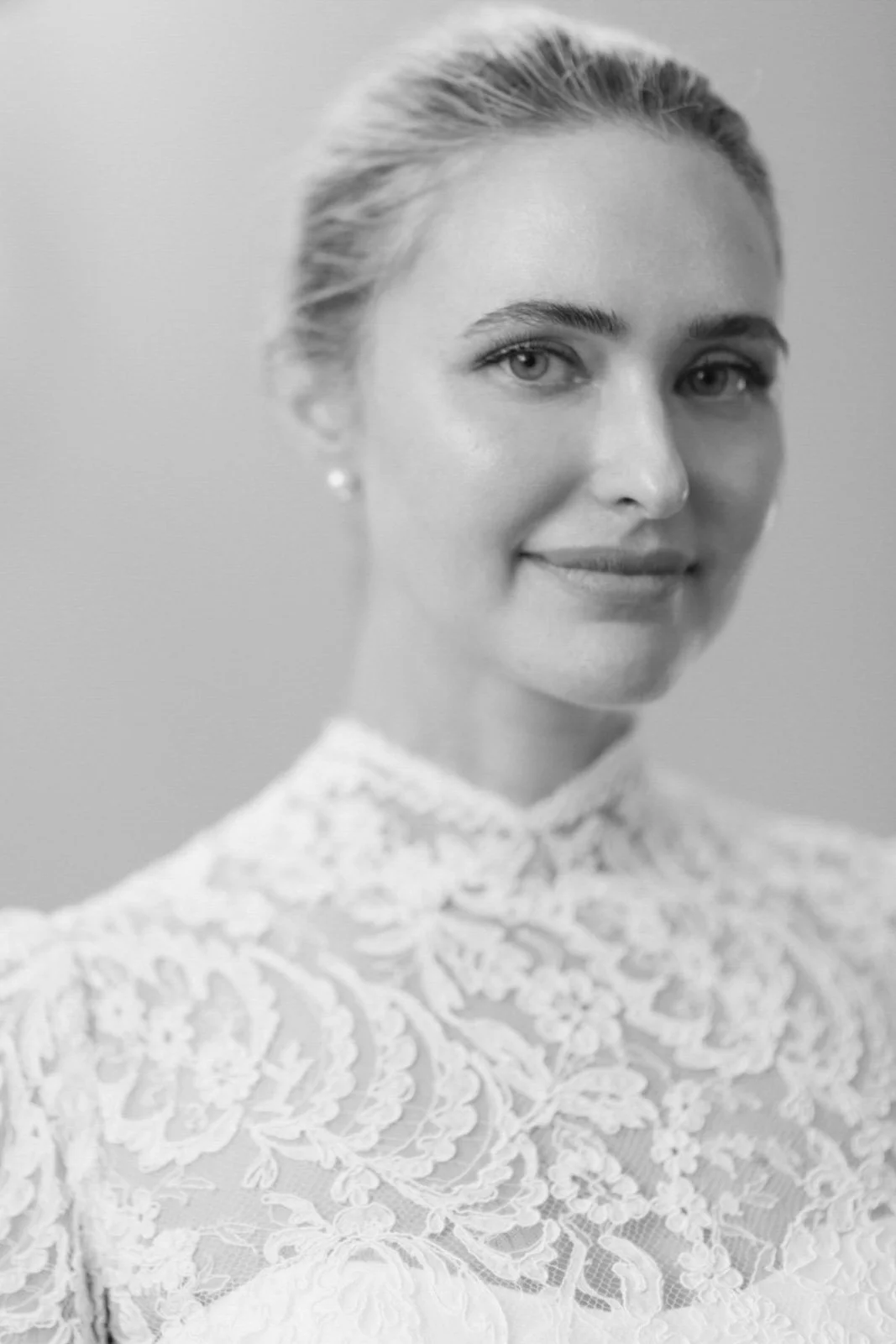 Black and white portrait of a woman with blonde hair, wearing a lace top and pearl earrings, smiling gently.