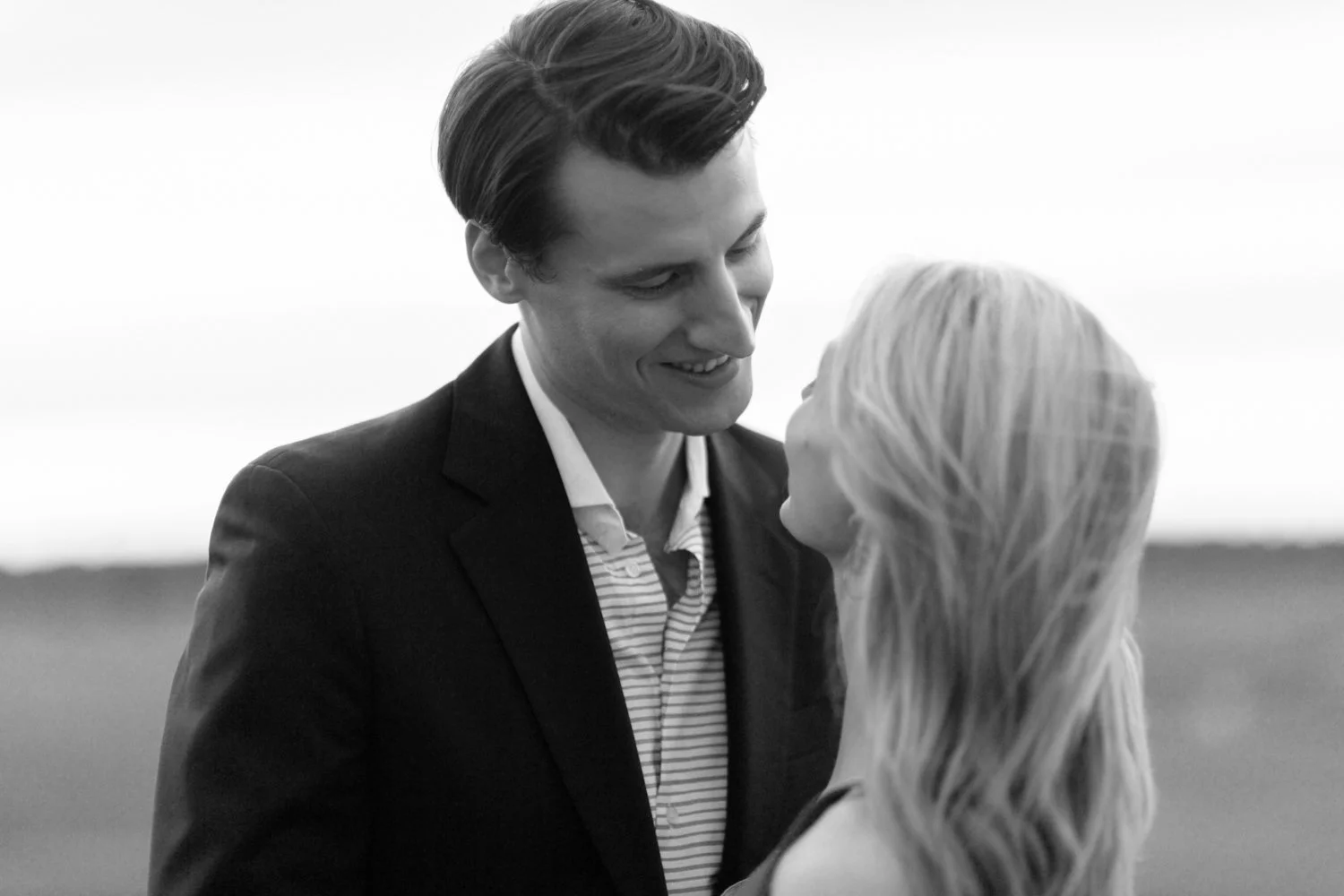 A black and white photo of a man and a woman, standing close together outdoors, smiling, with the man looking down at the woman.