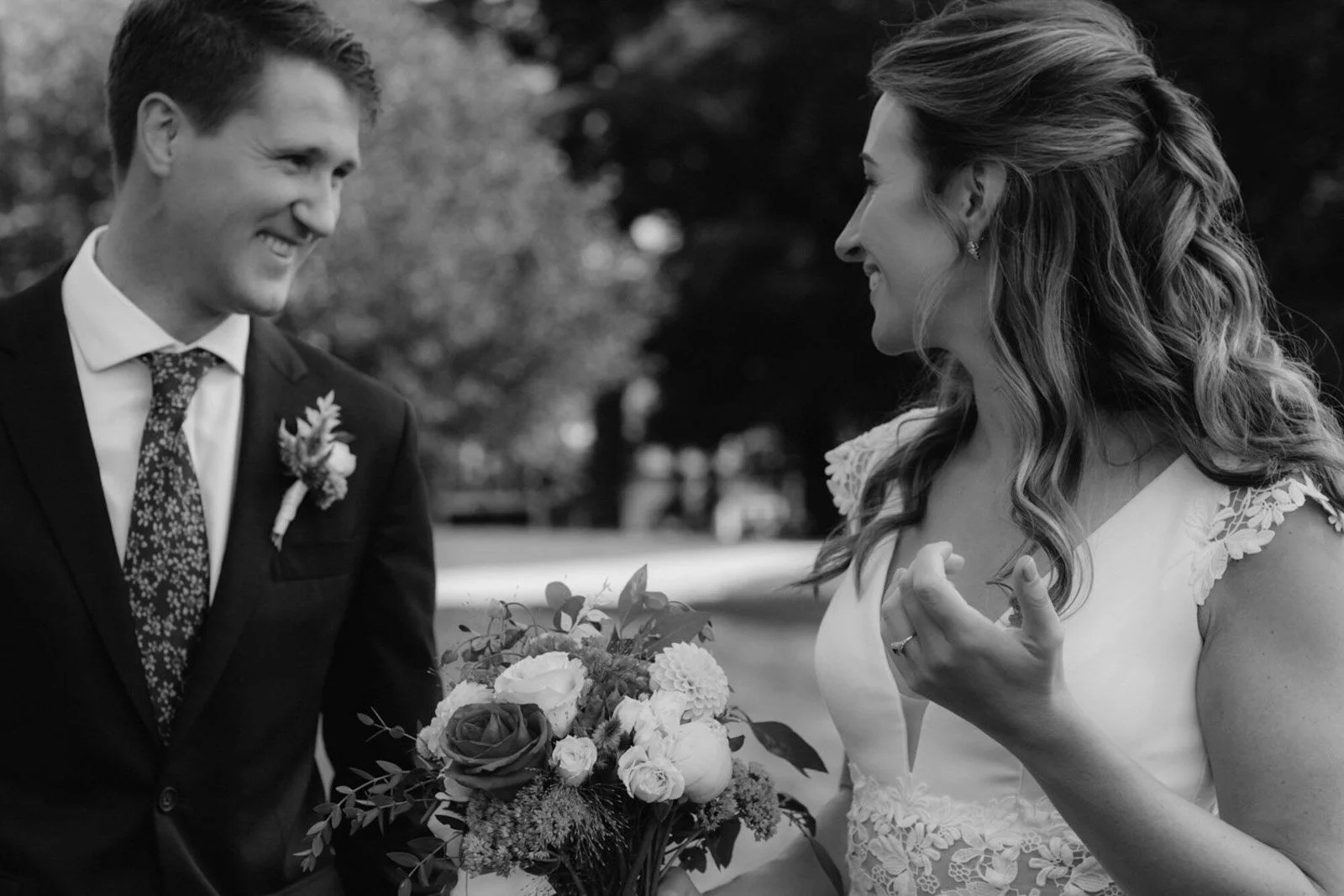 A black and white photo of a couple at their wedding, with the groom holding a bouquet and smiling at the bride, who is smiling back.