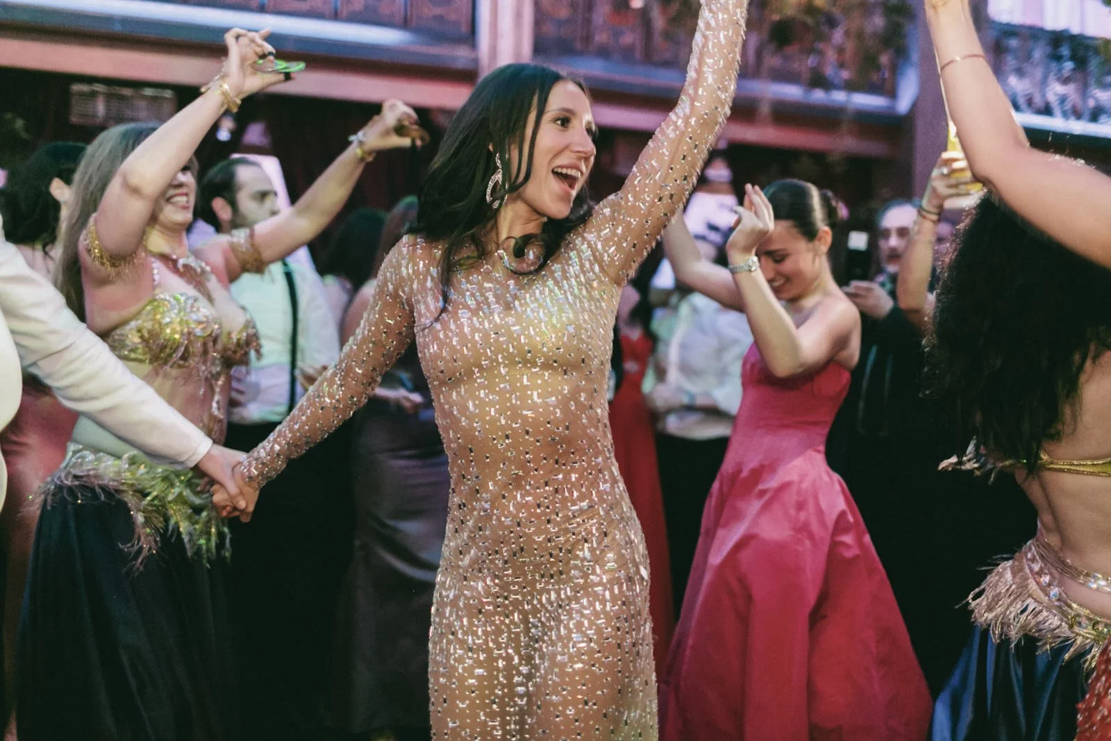 Group of women dancing and enjoying at a festive event, dressed in colorful and elegant dresses.