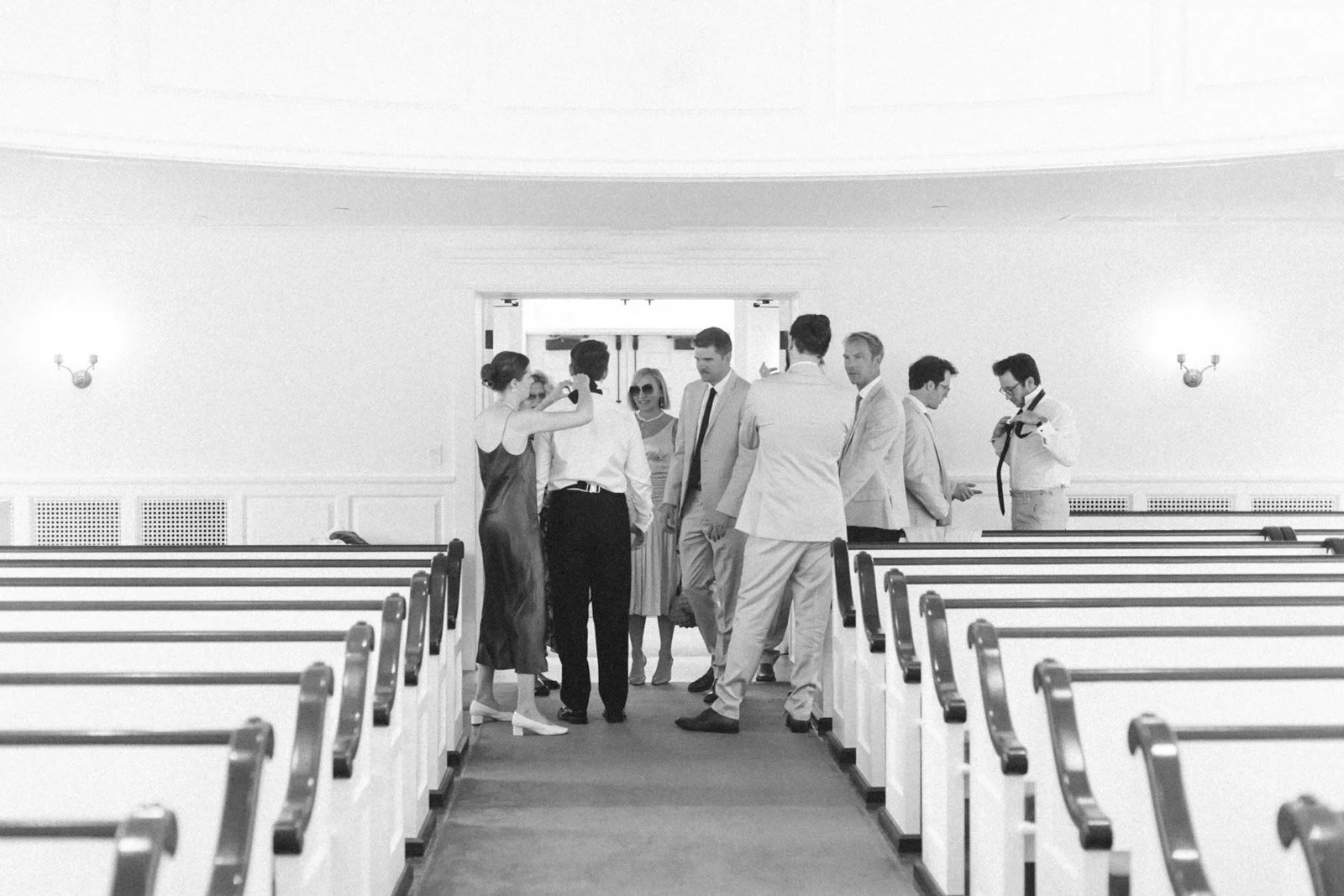 A group of people dressed in formal attire gathered in the aisle of a church, preparing for a wedding ceremony.