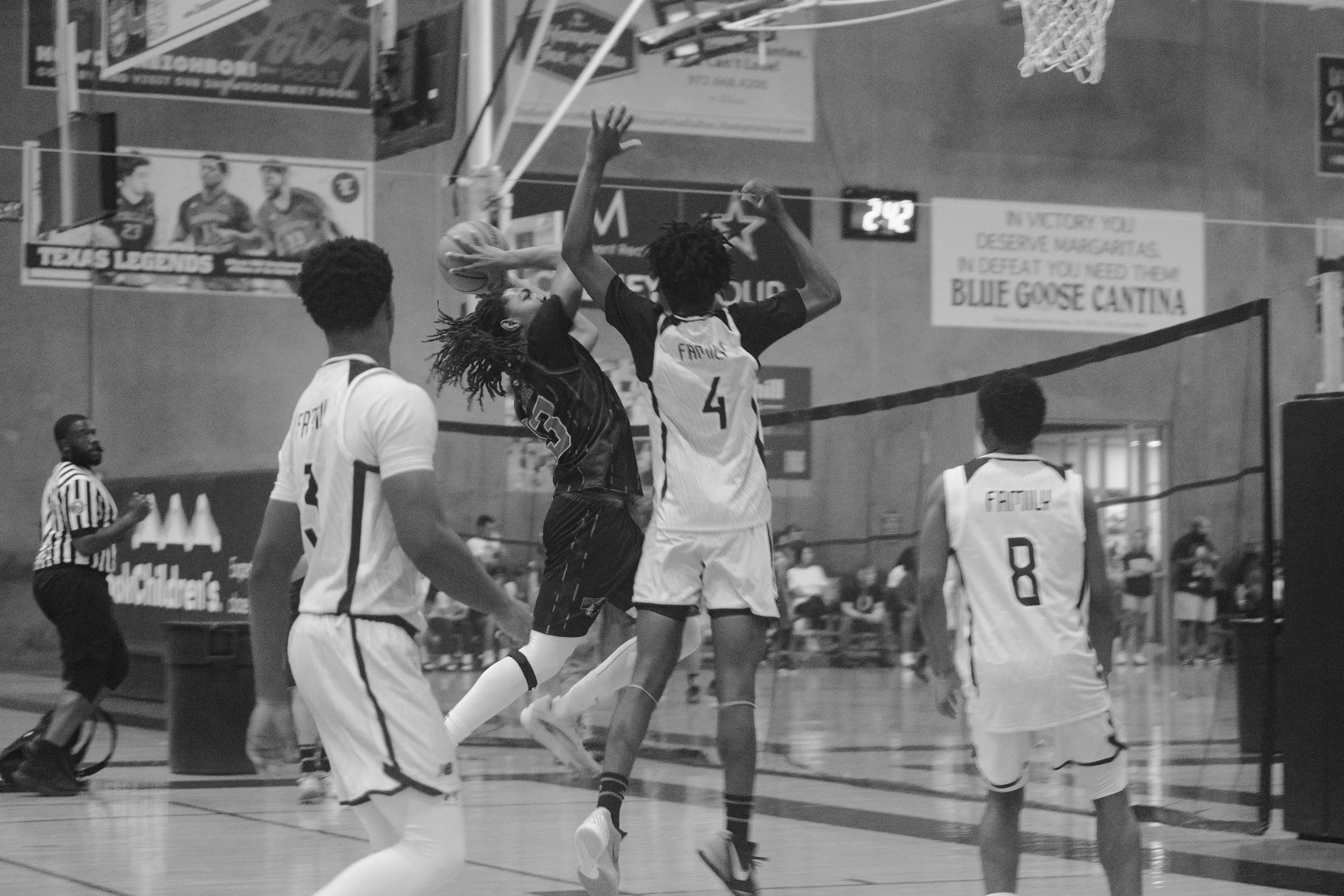 Black and white photo of a basketball game with players jumping for a ball near the hoop, in an indoor gymnasium.