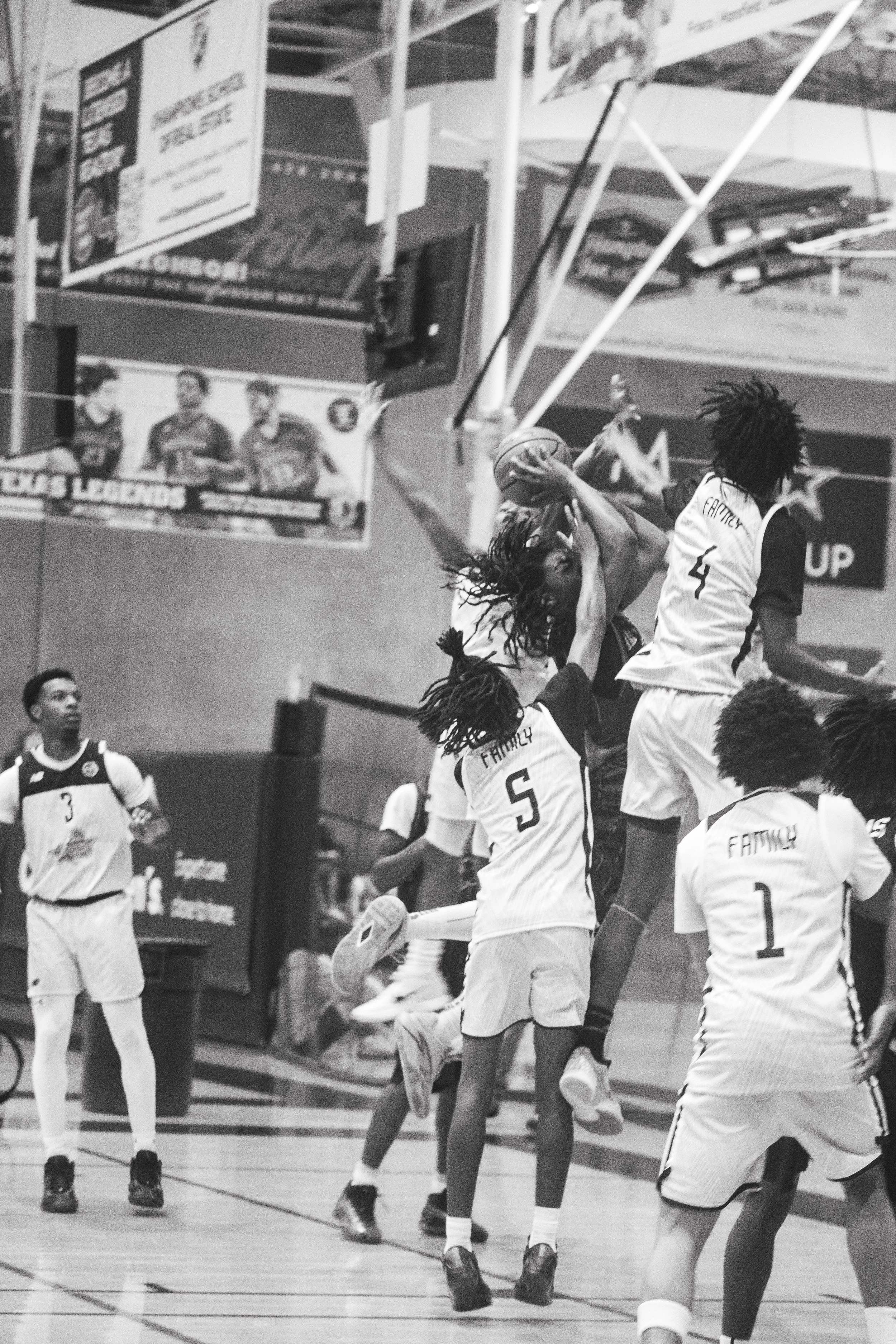 A group of female basketball players in action during a game, with some jumping to reach the ball near the basket, wearing uniforms with numbers and names, and other players on the court watching or preparing to jump.