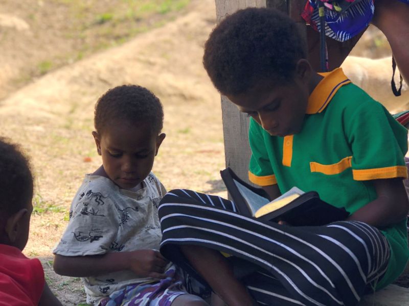 Menyan child reads the Bible as other kids sit and play
