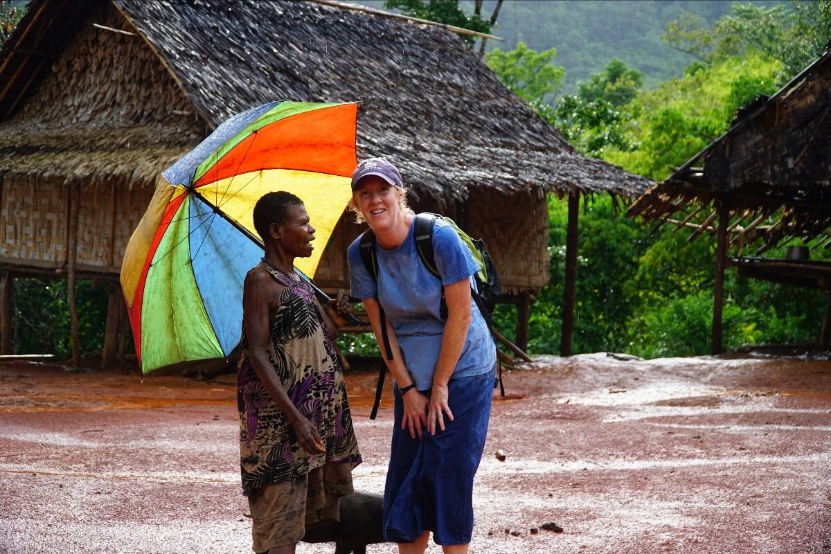 a missionary and her friend standing in the rain with an umbrella