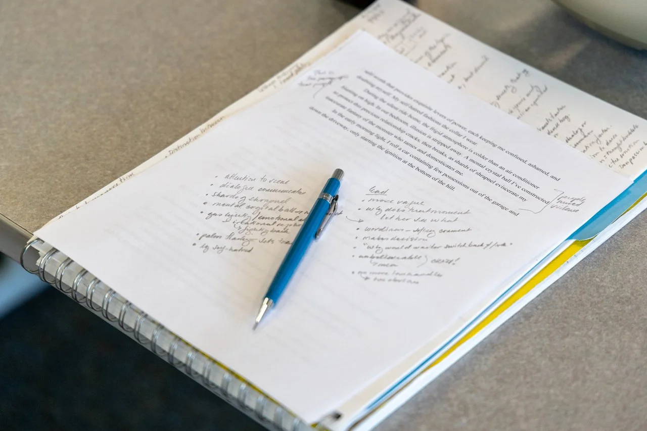 Open spiral-bound notebook or planner with handwritten notes and a blue pen resting on the page, placed on a gray table.